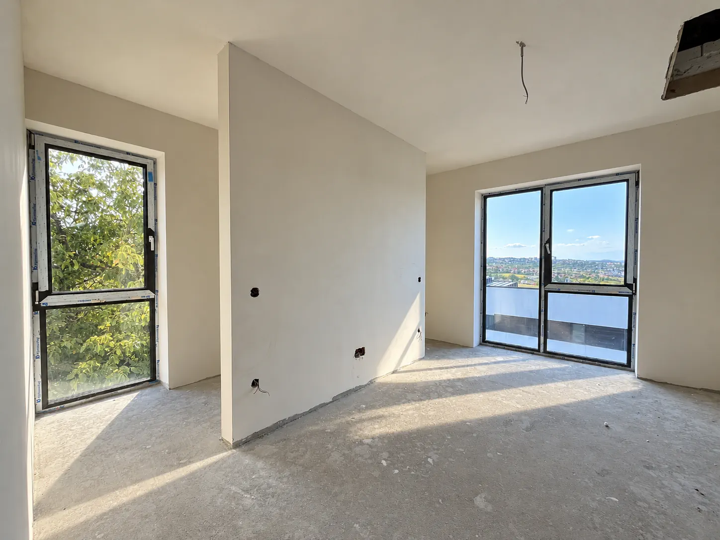 Dormitor cu ușă-fereastră spre balcon și fereastră spre copaci, pregătit pentru finisaje.
